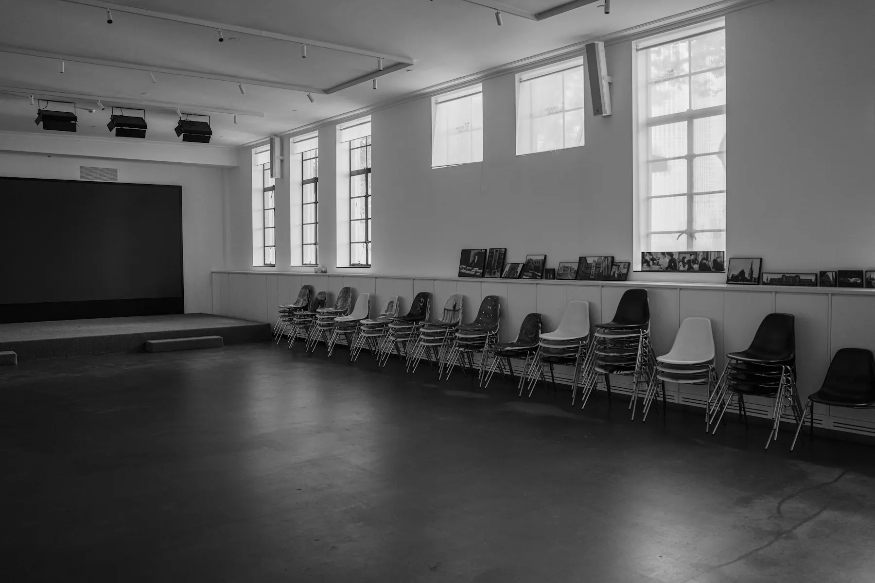A hall with a stage, tall windows and chairs stacked along the wall
