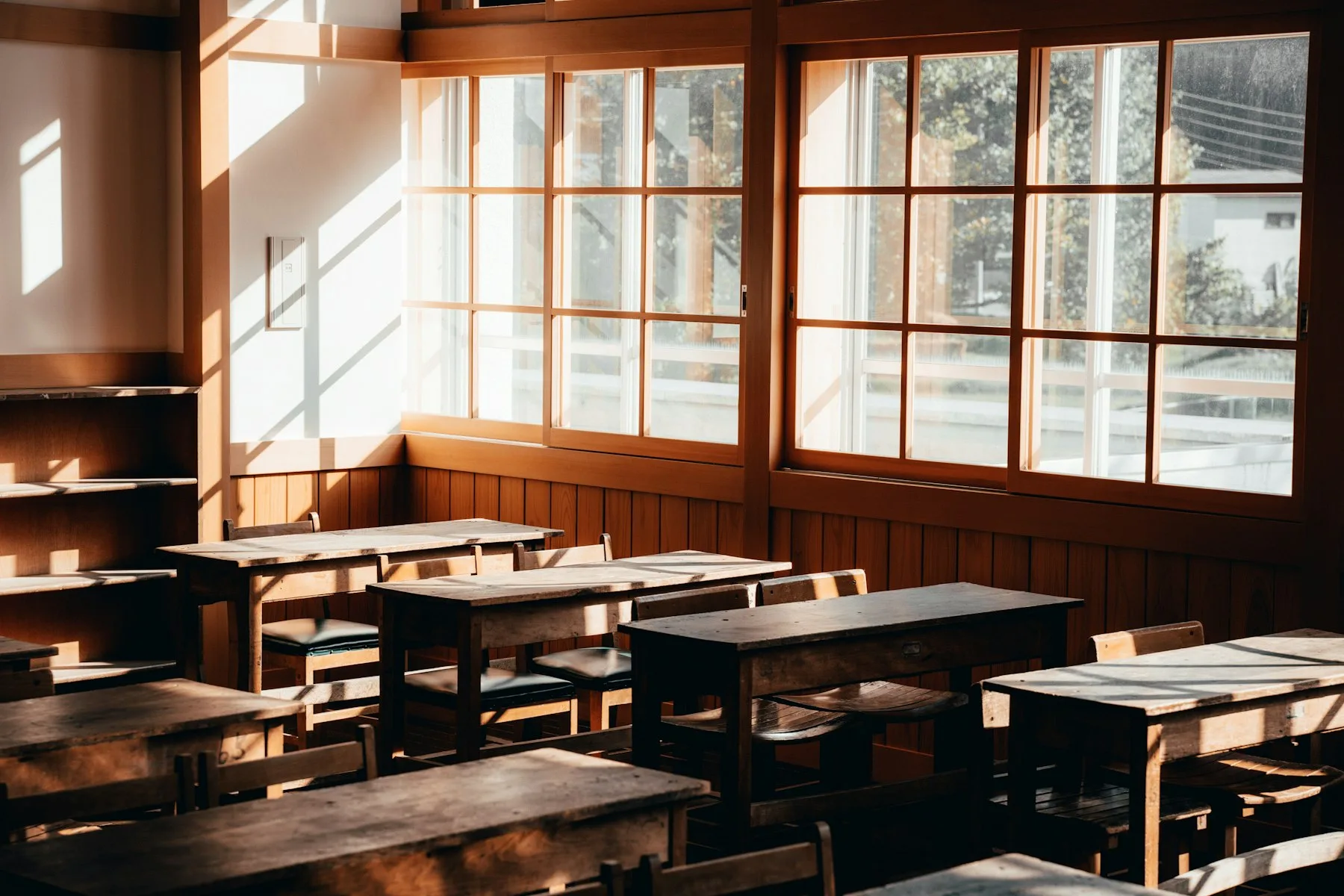 A sunlit classroom with empty wooden desks and chairs