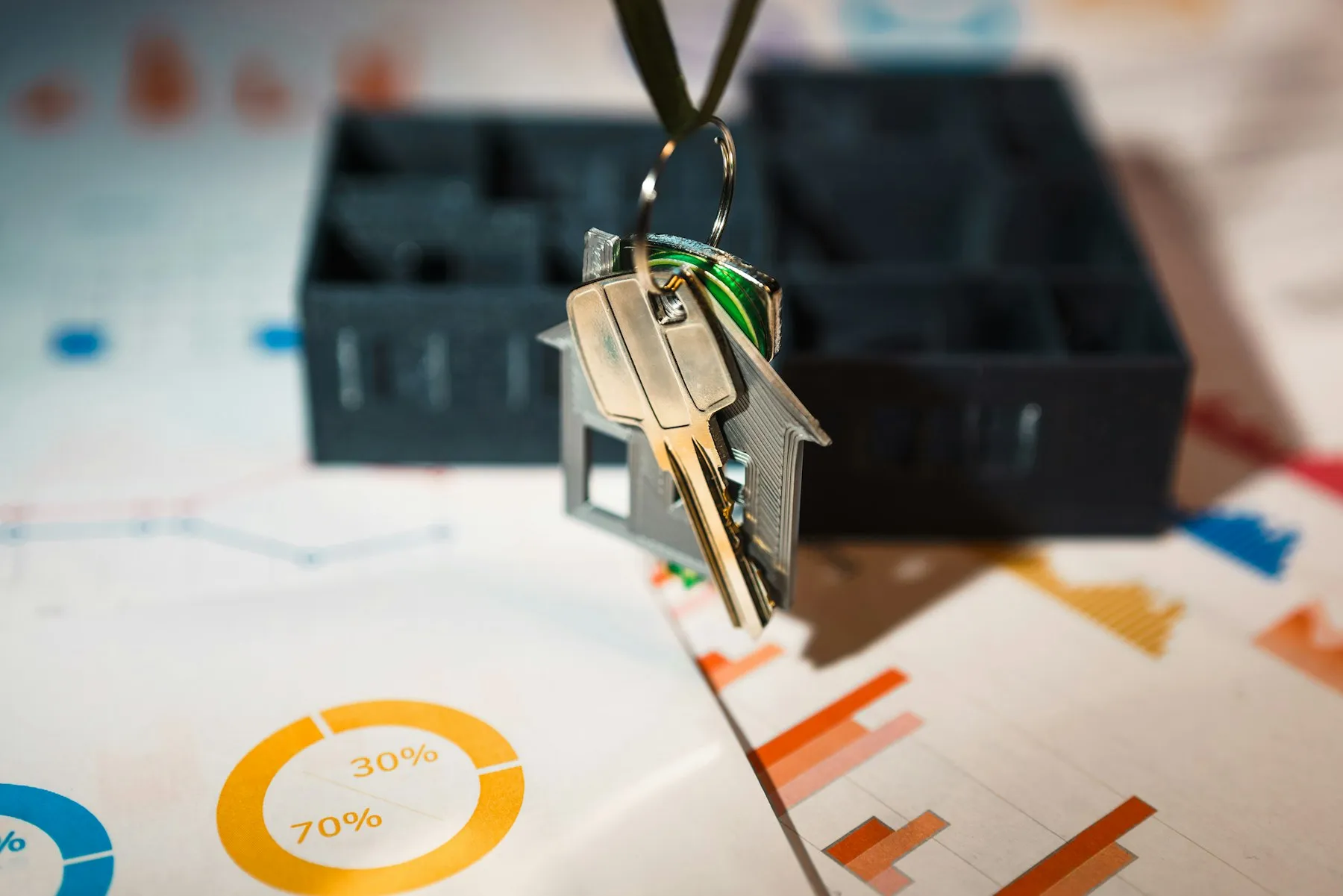 A set of house keys on a house-shaped fob in front of printed charts and a model home