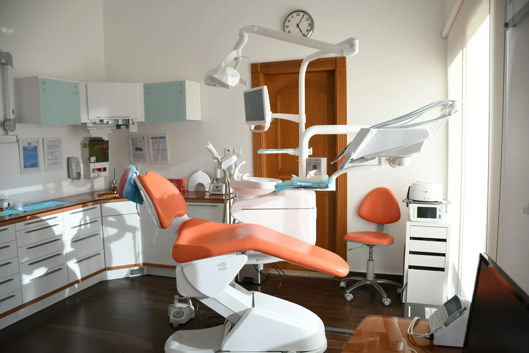 An empty dental surgery with an orange treatment chair, overhead light and wall cabinets