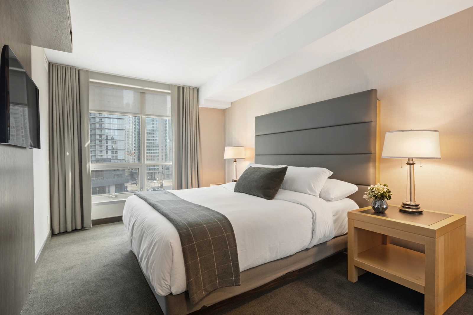 A hotel bedroom with white linen, a grey headboard and a window