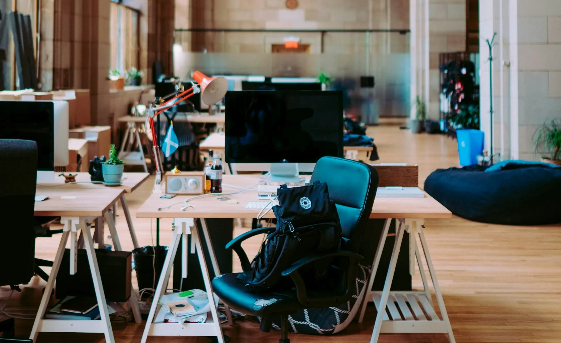 Open-plan desks with a switched-off monitor and an empty chair in a high-ceilinged converted hall