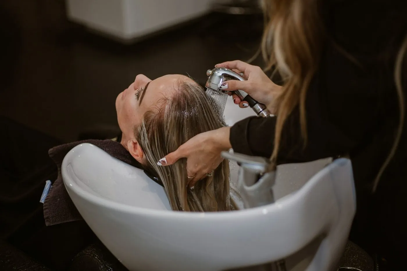 A hairdresser washing a client's hair at a basin